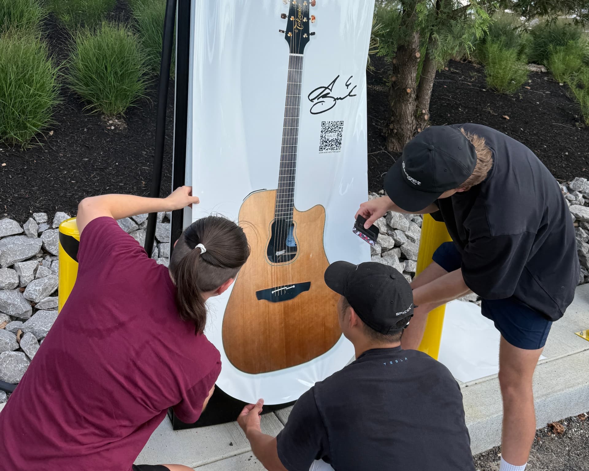 Crew installing a guitar-themed supercharger wrap on a commercial charging site in Tennessee